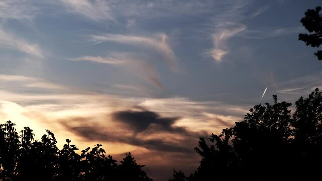 Mystical twilight sky over a quiet forest as dark clouds roll gently across the horizon. A jet passes quickly, leaving a contrail. Beautiful cinematic time-lapse &mdash; ideal for films, documentaries, or b