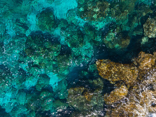 Aerial view of a rocky coastline in Ayia Napa, Cyprus, with vibrant turquoise and deep blue waters. Submerged and exposed rocks create intricate patterns.