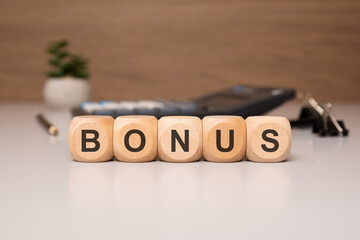 Wooden blocks spelling BONUS on an office desk with blurred office items in the background