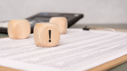 Wooden cube with exclamation mark on financial document, calculator in background