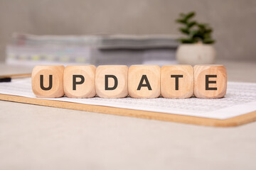 Wooden cubes spelling UPDATE on clipboard with financial sheets, office background