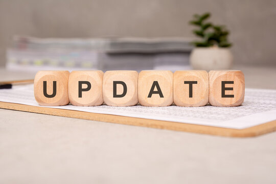 Wooden cubes spelling UPDATE on clipboard with financial sheets, office background