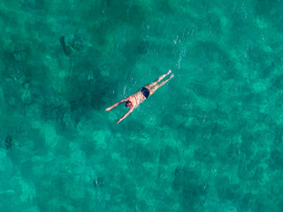 A person floats on their back in clear turquoise waters near Ayia Napa, Cyprus. The shallow sea reveals underwater textures, creating a serene scene.
