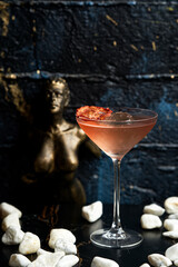 Pink Ice Cocktail with White Pebbles and Blurred Bronze Woman Statue in the Background