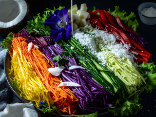 Colorful fresh vegetable salad platter with shredded carrots, purple cabbage, cucumber, red bell pepper, coconut, and garnished with edible flowers on a bed of green lettuce.Perfect for a healthy meal