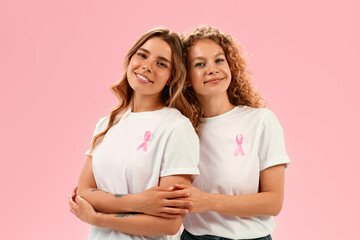 Two smiling women in white shirts with pink ribbons supporting breast cancer awareness