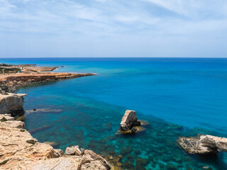 Ayia Napa coastline in Cyprus with turquoise waters, rugged rocky formations, sandy and rocky terrain, and a clear blue sky in the background.
