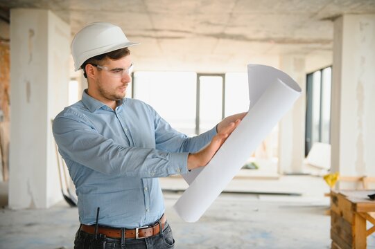 Portrait of an architect builder studying layout plan of the rooms, civil engineer working with documents on construction site