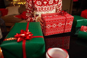 Woman wearing Christmas sweater holding wrapped Christmas gift with wrapping paper and ribbon...