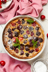 Cherry clafoutis in a white pan sprinkled with powdered sugar