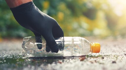 Volunteer hand picking up plastic bottle from wet asphalt puddle after rain slow motion ground view - Powered by Adobe