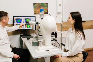 Ophthalmologist is showing corneal topography scan to girl patient near slit lamp. Diagnosis of the...