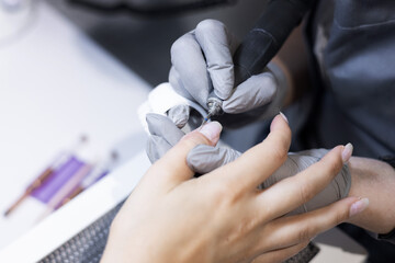 master applying gel polish on women nails in beauty salon. manicurist is polishing with file drill...