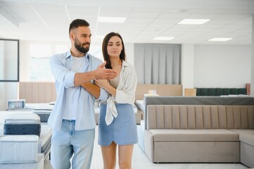 Fototapeta premium Couple of young man and woman shoppers choose comfortable sofa in department of furniture store