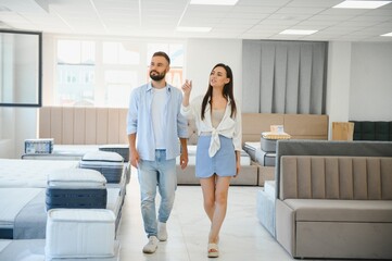 Couple of young man and woman shoppers choose sofa in living room department of furniture store