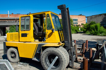 A bright yellow forklift stands idle at a construction site, surrounded by raw materials and machinery under a clear, blue sky