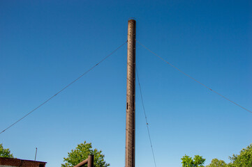 A tall wooden utility pole rises towards the clear blue sky in an urban setting, surrounded by...