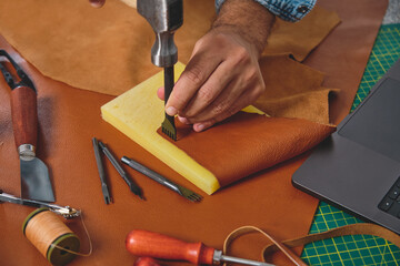 Craftsman using hammer and stitching groover tool on leather in workshop