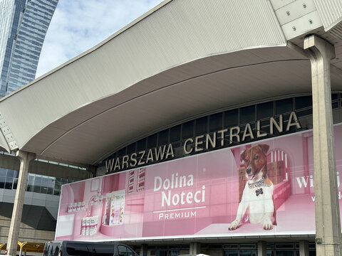 Warsaw, Poland - May 22, 2025: Warszawa Centralna train station exterior featuring large advertisement for Dolina Noteci dog food, showcasing vibrant branding and modern architecture