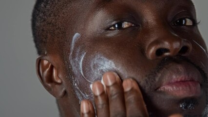 Close up view of young Black man applying moisturizing cream to his facial skin during daily self care routine - Powered by Adobe