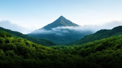 Naklejka premium A stunning mountain peak towers over verdant hills, shrouded in mist. The bright blue sky contrasts with the vibrant greenery, creating a serene landscape that invites exploration.