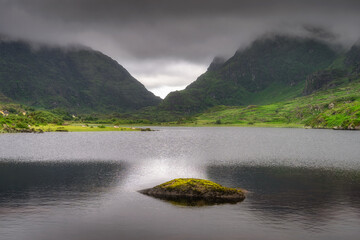 A tranquil and peaceful mountain lake, nestled within vibrant greenery of Gap of Dunloe, and under dramatic, fluffy clouds, beautifully capturing the serene beauty of nature, Kerry, Ireland