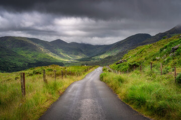 A winding road gracefully meanders through the vibrant green hills of Black Valley beneath a dramatic sky, perfectly showcasing the breathtaking beauty of this stunning landscape, Kerry, Ireland