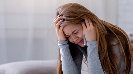 Sad young woman having conversation on mobile phone and crying at home. Millennial lady having...