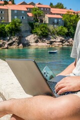 Man Working on Laptop at Beach with View of Sveti Stefan Island, Montenegro — Remote Tech Job, Digital Nomad Lifestyle, Cloud Computing, Freelancing in Paradise