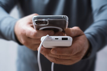 Close-up of a man holding a power bank and charging a smartphone. Portable charger for phone and gadgets.