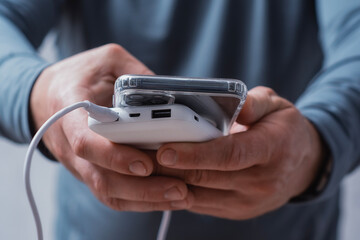 Close-up of a man holding a power bank and charging a smartphone. Portable charger for phone and...