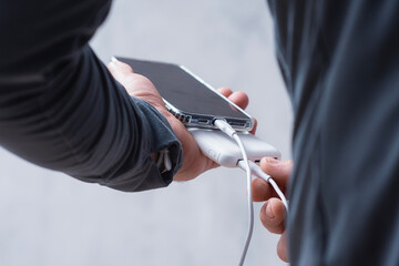 Close-up of a man holding a power bank and charging a smartphone. Portable charger for phone and...