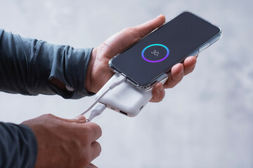 Close-up of a man holding a power bank and charging a smartphone. Portable charger for phone and gadgets.