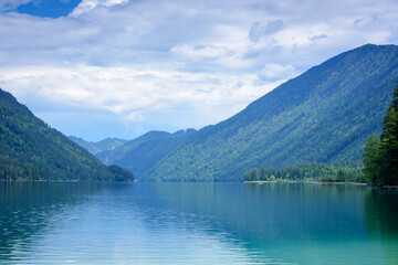 View of a lake with green hills in the distance and cloudy sky