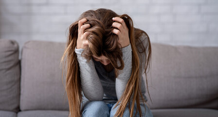 Desperate young woman sitting head in hands on sofa and crying, panorama. Upset lady thinking about problem or having depression, suffering from nervous breakdown. Mental health concept