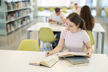 Female university student reads a book and writes in a notebook. Students prepare for university