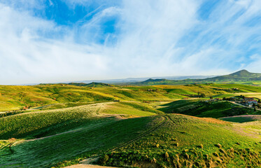green agricultural spring or summer landscape of grassland hills near small village with young grass and amazing cloudy sky