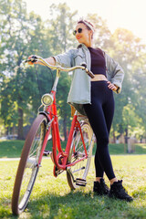 Portrait young adult pretty woman with red vintage retro bike and pin-up casual outfit green city park bright sunny summer day. Happy beautiful female person cycling outdoors. Healthy lifestyle