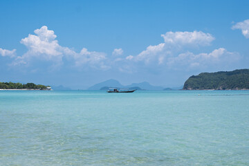 Fototapeta premium Landscape photo of a Thai longtail boat from the paradise island of Pig Island (Koh Madsum) in Koh Samui. Beautiful tropical landscape with turquoise blue water and lush vegetation, on a beautiful sun