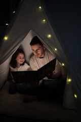 Father reading bedtime story to daughter in teepee tent © asier