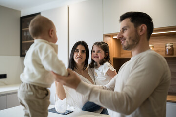 Happy family playing with baby and toddler in kitchen