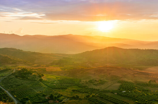 scenic rustic landscape with green hills and farms in a mountain valley during colorful cloudy sunset