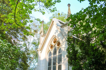 Gothic revival church tower with pointed arch windows surrounded by green trees in springtime