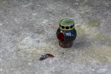 A dark, red-tinged glass memorial lamp with a flickering flame sits on a grey concrete surface.