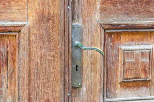 A detailed close-up of an old, weathered wooden door with a rustic metal handle and carved accents.