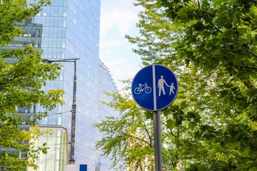 A blue circular sign with a white bicycle symbol, indicating a bicycle path or designated cycling area, against green foliage.