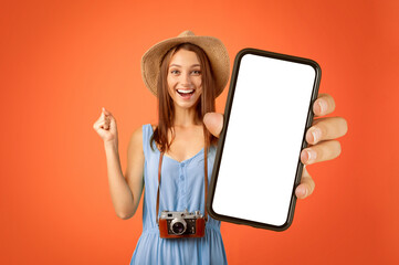 Emotional girl traveller with camera showing smartphone with empty screen, yellow studio background