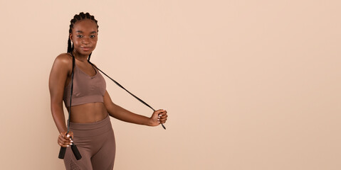 Portrait Of Happy Young Sporty Black Woman Holding Jump Rope, Millennial African American Female In Sportswear Ready For Fitness Training, Posing Isolated Over Beige Background, Copy Space