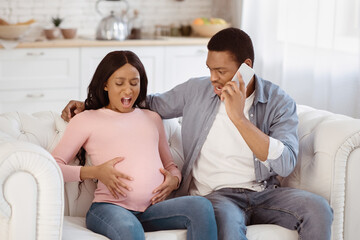 Expectant black woman having prenatal contractions, her boyfriend reaching doctor on smartphone...