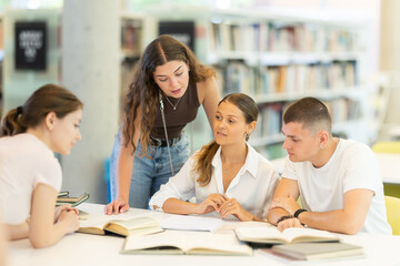 Group of students talking, reading books and taking notes at table in library